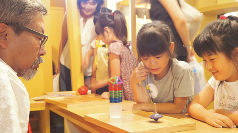 学芸員が子供たちと木のコマで遊んでいる様子