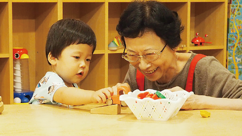 学芸員が小さな子供と木の車で遊んでいる様子